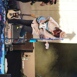 Gitarrist im Einsatz. Er hat das linke Bein angewinkelt und ist nach links gelehnt. Als würde er vom rechten aufs linke Bein wechseln.