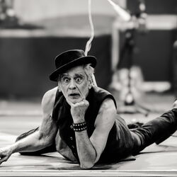 Das schwarz-weiß Bild zeigt Melingo, wie er auf dem Bauch liegt und seinen Kopf auf dem linken arm abstützt. Seine Augen sind weit aufgerissen und er trägt einen Hut.