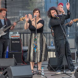 Das Bild zeigt 4 Musiker auf der Bühne. Im Vordergrund 2 Sänger, welche jeweils in eine andere Richtung gedreht sind und ihre Hände heben um zu klatschen. Im Hintergrund stehen zwei Gitarristen.