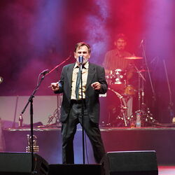 Ein Sänger im schicken, schwarzen Anzug. Im Hintergrund auf einer Erhöhung der Schlagzeuger.