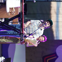 Ein Mann steht am Keyboard, dieser singt zusätzlich noch. Im Hintergrund steht ein Mann im grünen Anzug mit Saxophon  in der Hand.